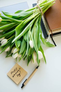Beyaz laleler buketi ve yapışkan bir notla 8 Mart 'ta iş yeri masası manzarası üzerine yatıyorsun.