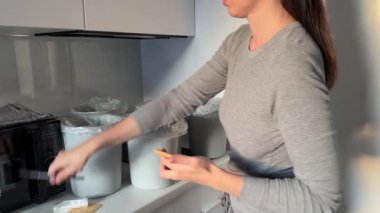 Evdeki atık tasnif organizasyonu. Tüketime karşı bilinçli yaklaşım, ekolojik sorumluluk, sürdürülebilir yaşam hacklemeleri. Evdeki atık ayrımını düzenleyen kadın.