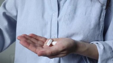 Kadın hapları yakından alıyor. Kadınların elinde iki büyük beyaz tablet.