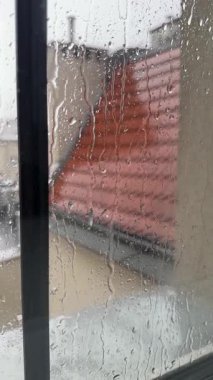 Yağmur sırasında içeriden bir daire penceresi. Son katın penceresine kiremit çatı manzaralı yağmur damlaları düşüyor. Kötü yağmurlu, karamsar hava, hüzünlü hava, sakinlik ve rahatlama.