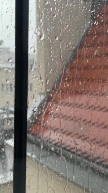Yağmur sırasında içeriden bir daire penceresi. Son katın penceresine kiremit çatı manzaralı yağmur damlaları düşüyor. Kötü yağmurlu, karamsar hava, hüzünlü hava, sakinlik ve rahatlama.