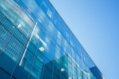 Yansıtıcı camdan yapılmış modern ofis binası cephesi. Ticari mülkiyet dışı. Finans bölgesi gökdelenlerinin yansıması, açık mavi gökyüzü arkaplanı.