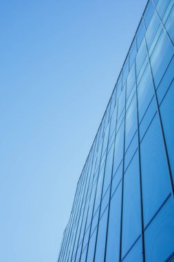 Cam ve açık mavi gökyüzünden yapılmış yansıtıcı ofis binası cephesi. Minimalist soyut geometrik desen. Çağdaş arkaplan, modern dış görünüş, kentsel mimari.