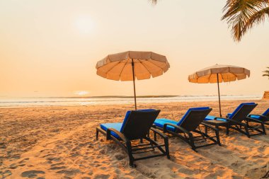 Güneş doğarken palmiye ağacı ve deniz plajı olan şemsiye koltuğu plajı - tatil ve tatil konsepti
