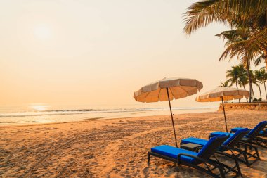 Güneş doğarken palmiye ağacı ve deniz plajı olan şemsiye koltuğu plajı - tatil ve tatil konsepti