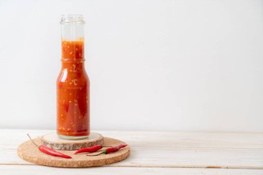 Şişede kırmızı biber ya da kırmızı biber sosu ve arka planda kavanoz.