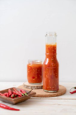 Şişede kırmızı biber ya da kırmızı biber sosu ve arka planda kavanoz.