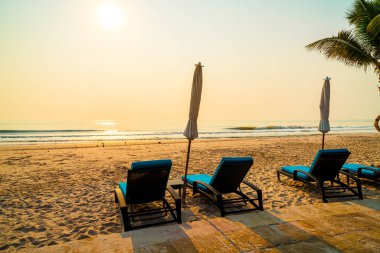 Güneş doğarken palmiye ağacı ve deniz plajı olan şemsiye koltuğu plajı - tatil ve tatil konsepti