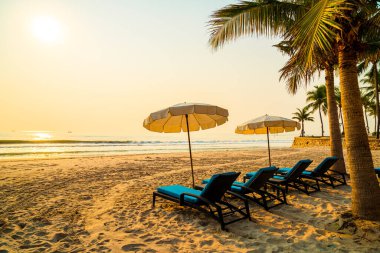 Güneş doğarken palmiye ağacı ve deniz plajı olan şemsiye koltuğu plajı - tatil ve tatil konsepti