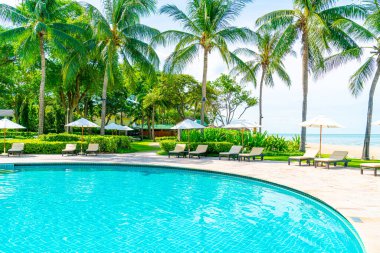 Güzel tropikal plaj ve deniz şemsiyesi ve sandalyesi otel tatil ve tatil için yüzme havuzunda.