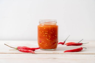 Şişede kırmızı biber ya da kırmızı biber sosu ve arka planda kavanoz.
