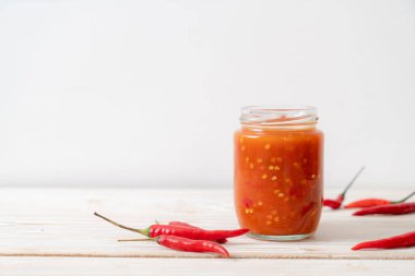 Şişede kırmızı biber ya da kırmızı biber sosu ve arka planda kavanoz.