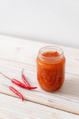 Şişede kırmızı biber ya da kırmızı biber sosu ve arka planda kavanoz.
