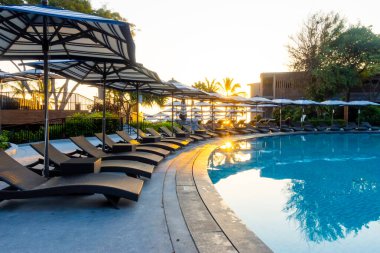 Şemsiye ve sandalye, gün batımında veya gökyüzünde güneşli bir tatil için otel tatil beldesinde yüzme havuzunun etrafında.