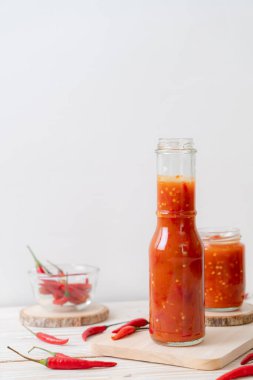 Şişede kırmızı biber ya da kırmızı biber sosu ve arka planda kavanoz.