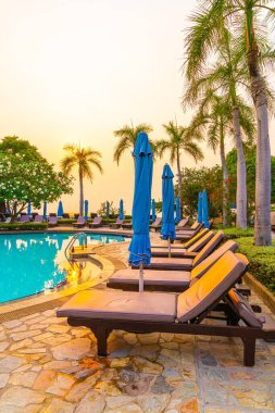 Gün batımında yüzme havuzunda şemsiyeli plaj sandalyesi ya da bilardo yatağı