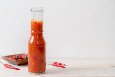 Şişede kırmızı biber ya da kırmızı biber sosu ve arka planda kavanoz.