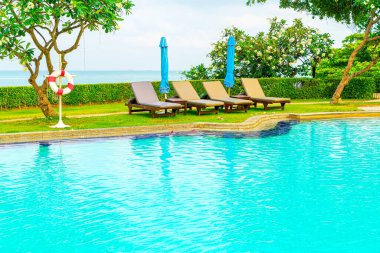 Sandalye havuzu ve şemsiyeyle okyanus arka planında yüzme havuzu