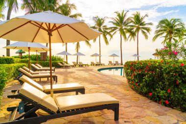 Şemsiye ve sandalye tatil ve tatil için dinlenme yeri otelinde yüzme havuzunda günbatımında veya gün doğumunda okyanus kıyısında