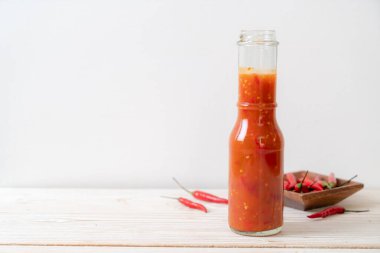 Şişede kırmızı biber ya da kırmızı biber sosu ve arka planda kavanoz.