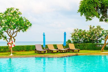 Sandalye havuzu ve şemsiyeyle okyanus arka planında yüzme havuzu