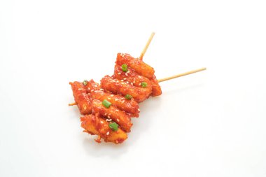 Kızarmış Kore pirinç keki (Tteokbokki) beyaz arka planda izole edilmiş baharatlı sosla şişlenmiş.