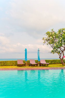 Sandalye havuzu ve şemsiyeyle okyanus arka planında yüzme havuzu