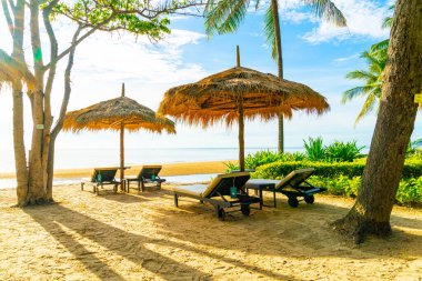 Şemsiye ve sahil sandalyesi Hindistan cevizi palmiyesi ve deniz plajı arka planı ve mavi gökyüzü - tatil ve tatil kavramı