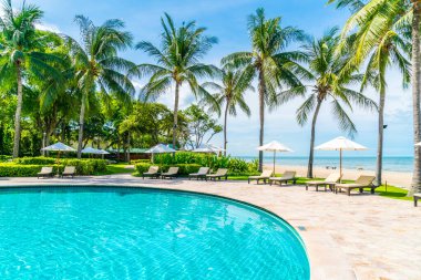 Güzel tropikal plaj ve deniz şemsiyesi ve sandalyesi otel tatil ve tatil için yüzme havuzunda.