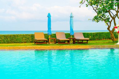 Sandalye havuzu ve şemsiyeyle okyanus arka planında yüzme havuzu