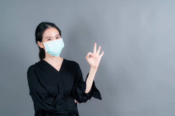 Young Asian woman wearing medical face mask protects filter dust pm2.5 anti-pollution, anti-smog, COVID-19 and showing OK sign