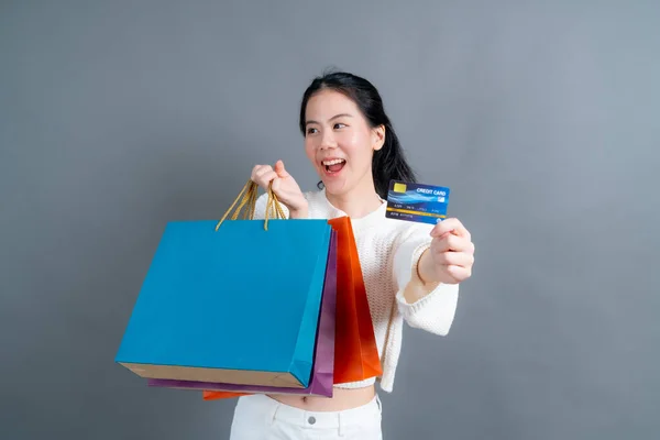 美しいアジアの女性でショッピングバッグと表示クレジットカード絶縁上グレーの背景 — ストック写真