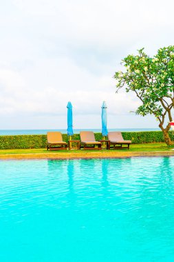 Sandalye havuzu ve şemsiyeyle okyanus arka planında yüzme havuzu
