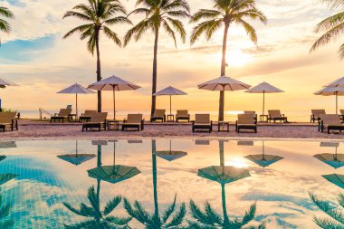 Şemsiye ve sandalye tatil ve tatil için dinlenme yeri otelinde yüzme havuzunda günbatımında veya gün doğumunda okyanus kıyısında