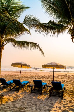 Güneş doğarken palmiye ağacı ve deniz plajı olan şemsiye koltuğu plajı - tatil ve tatil konsepti