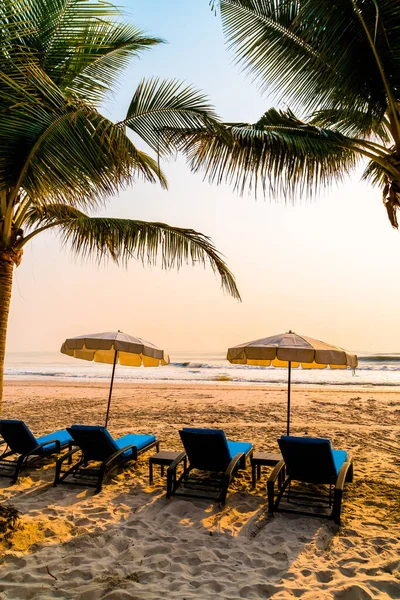 Güneş doğarken palmiye ağacı ve deniz plajı olan şemsiye koltuğu plajı - tatil ve tatil konsepti