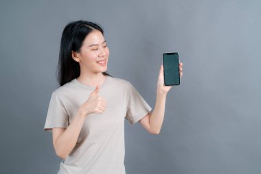 Cep telefonu uygulamaları kullanan Asyalı kadın, sosyal ağda uzaktan iletişim kurmaktan zevk alıyor ya da gri arka planda izole edilmiş alışveriş yapıyor.