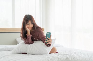 Güzel Asyalı kadınlar yatakta akıllı telefon oynuyorlar.