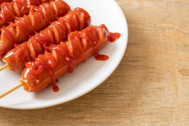 Beyaz tabakta ketçaplı kızarmış sosis şişi.