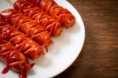 Beyaz tabakta ketçaplı kızarmış sosis şişi.