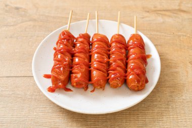 Beyaz tabakta ketçaplı kızarmış sosis şişi.