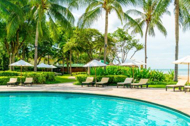 Güzel tropikal plaj ve deniz şemsiyesi ve sandalyesi otel tatil ve tatil için yüzme havuzunda.