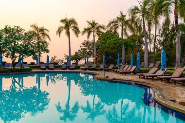 Gün batımında yüzme havuzunda şemsiyeli plaj sandalyesi ya da bilardo yatağı