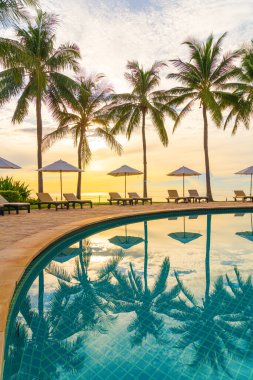 Şemsiye ve sandalye tatil ve tatil için dinlenme yeri otelinde yüzme havuzunda günbatımında veya gün doğumunda okyanus kıyısında