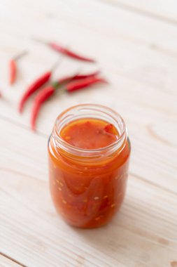 Şişede kırmızı biber ya da kırmızı biber sosu ve arka planda kavanoz.