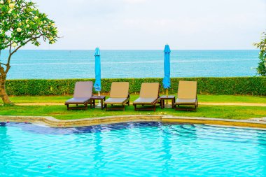 Sandalye havuzu ve şemsiyeyle okyanus arka planında yüzme havuzu