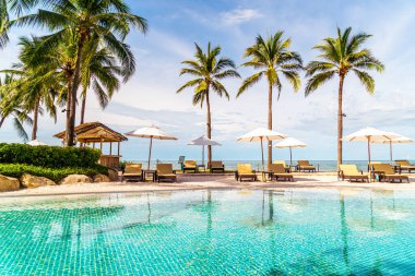 Güzel tropikal plaj ve deniz şemsiyesi ve sandalyesi otel tatil ve tatil için yüzme havuzunda.