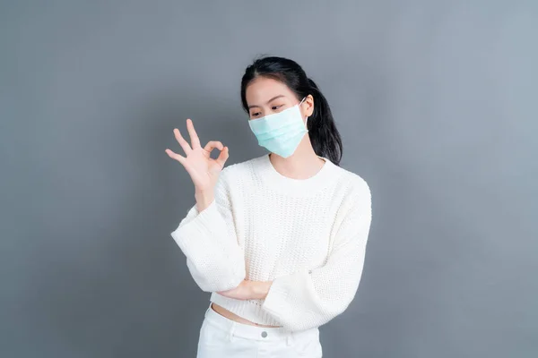 Young Asian woman wearing medical face mask protects filter dust pm2.5 anti-pollution, anti-smog, COVID-19 and showing OK sign