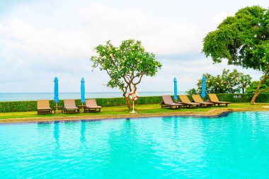 Sandalye havuzu ve şemsiyeyle okyanus arka planında yüzme havuzu