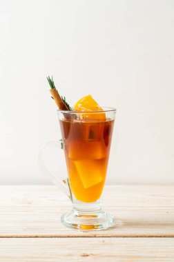 Bir bardak buzlu americano sade kahve ve ahşap arka planda biberiye ve tarçınla süslenmiş portakal ve limon suyu.